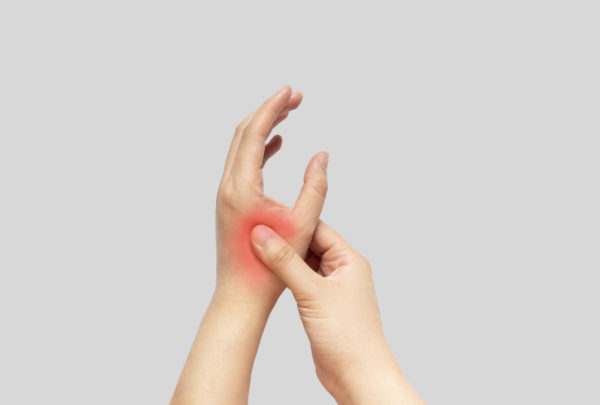 Young female suffering from pain in hands and massaging her painful hands isolated gray background. Causes of hurt include carpal tunnel syndrome, fractures, arthritis, gout attack or trigger finger.
